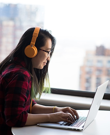 Ein Mädchen hört Musik und sitzt dabei am Laptop